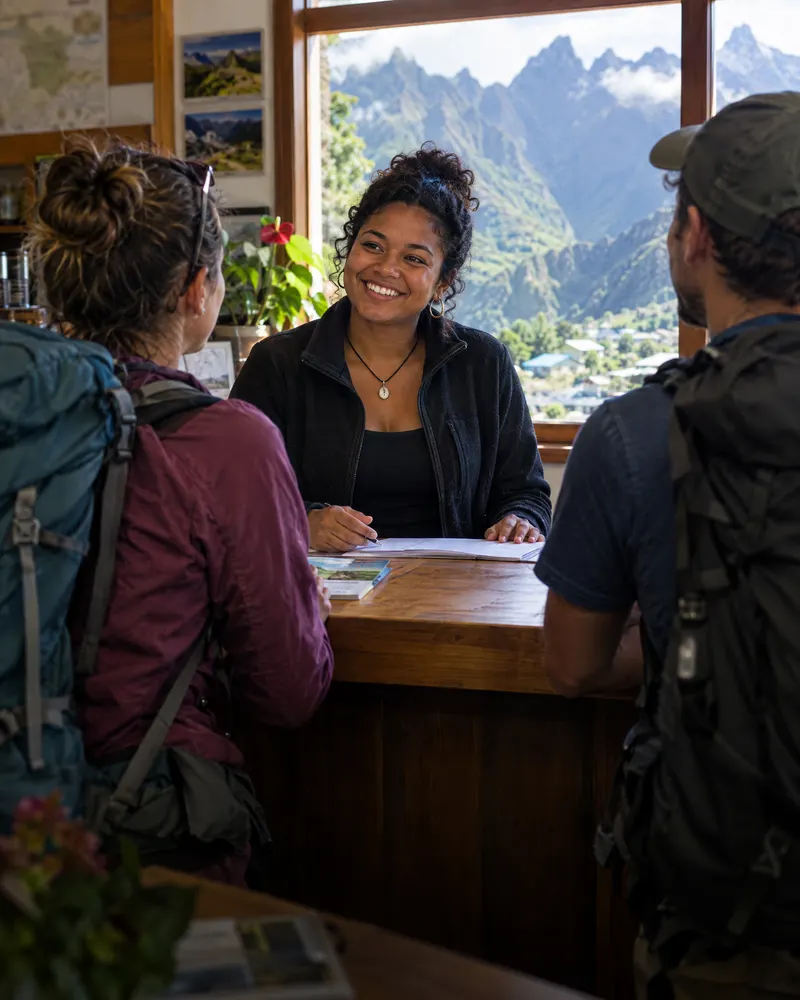 Réceptionniste souriante qui accueille deux randonneurs, montagnes en arrière-plan